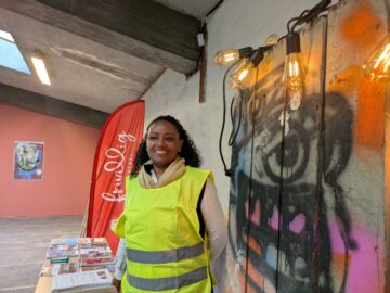 Daglig leder for frivilligsentralen foran infostand og flagg med logo